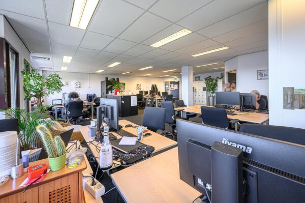 Moderne, open kantoortuin in gebouw De Linie met werkplekken, computers en planten.